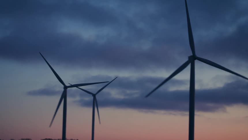 Several towering wind turbines spin slowly under a cloudy sky