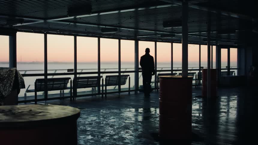 Silhouette of a man facing away inside a establishment observing the sea view under a pink dawn sky