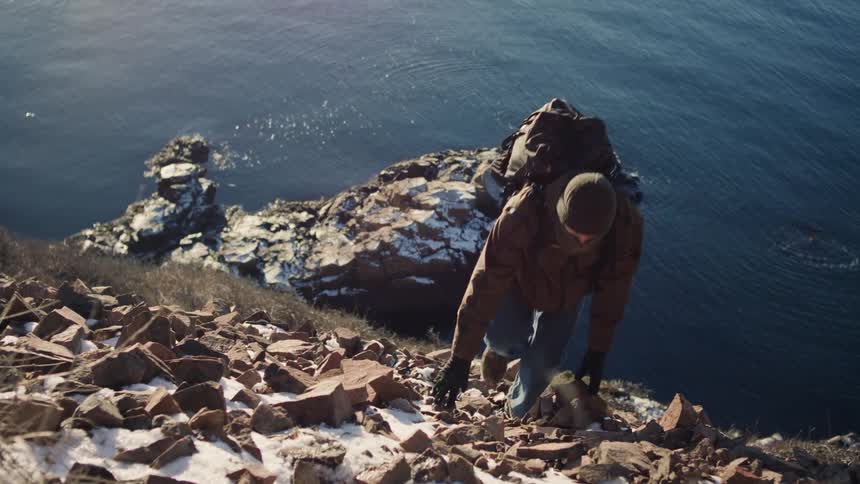 A backpacker climbing a steep rocky hill by the sea