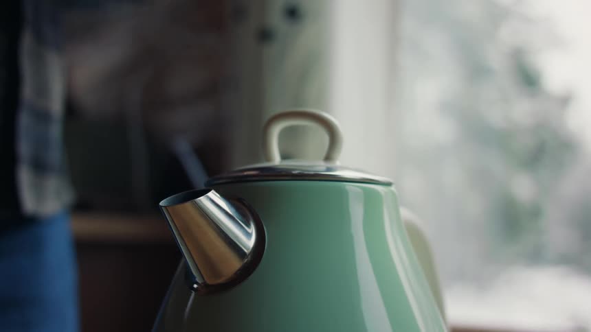 Close up of a metallic green teapot steaming at home