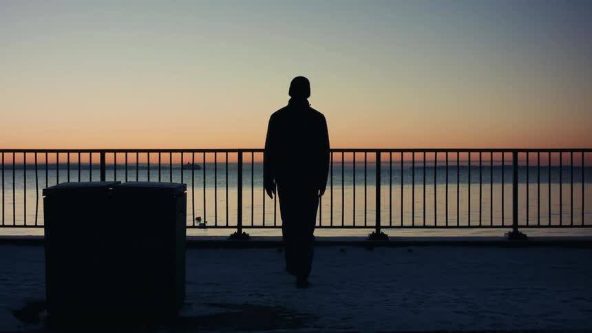 Man walking towards a fence by the seaside on a winter morning