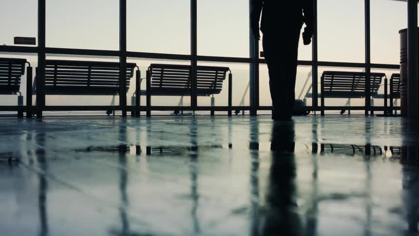 A man slowly walks towards a row of benches next to a large window