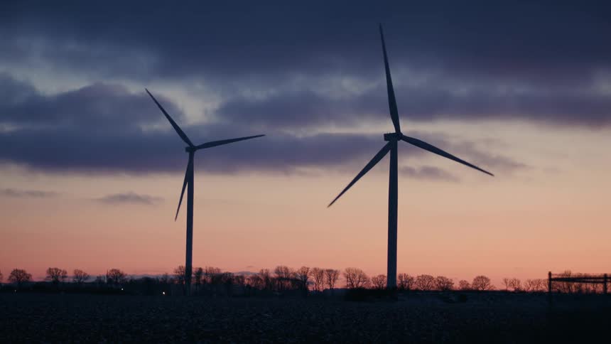 Two wind turbines turn slowly under a red tinted sky on a cloudy winter day