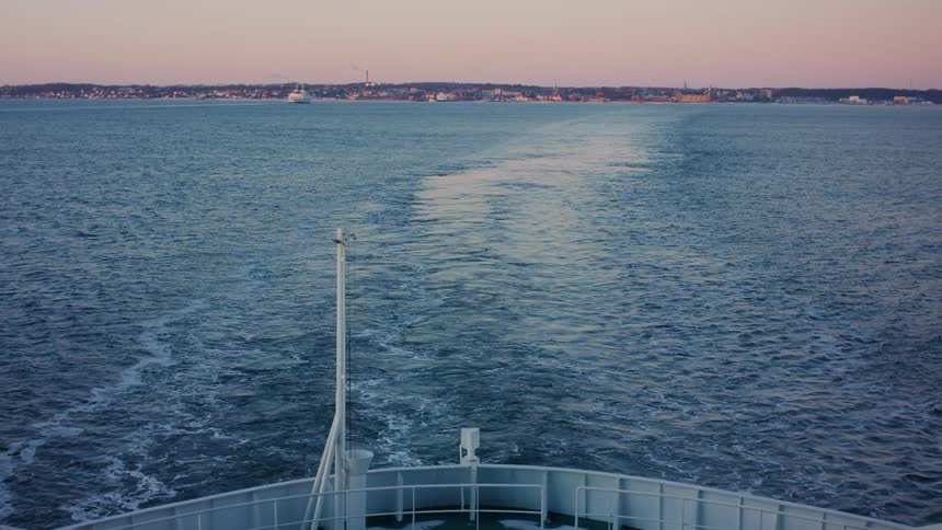 A large boat steadily travels away from a coastline on an overcast day