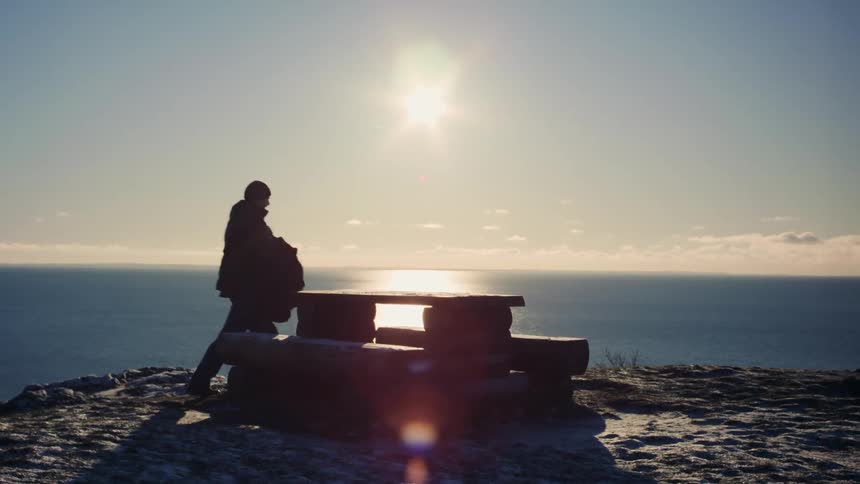 Backpacker sits on picnic table on promonotry on sunny winter day