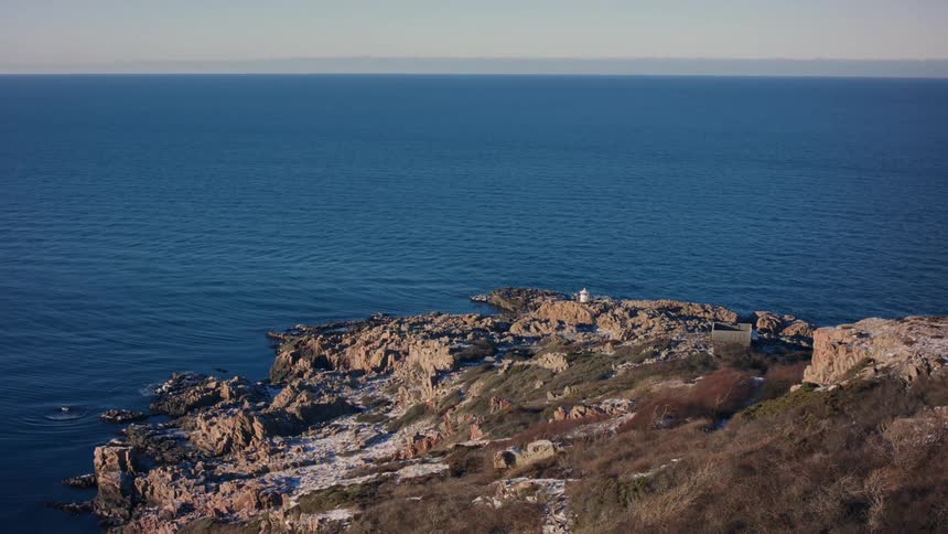 A rocky cliff overlooks the serine blue ocean on a sunny day