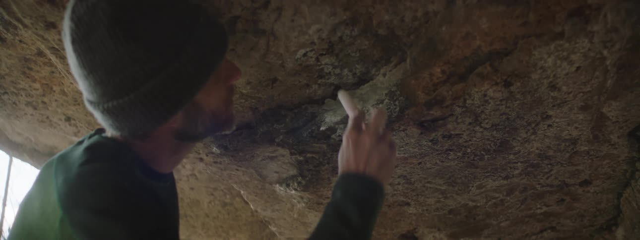 A man using a brush to clean a ridge on the underside of a rock