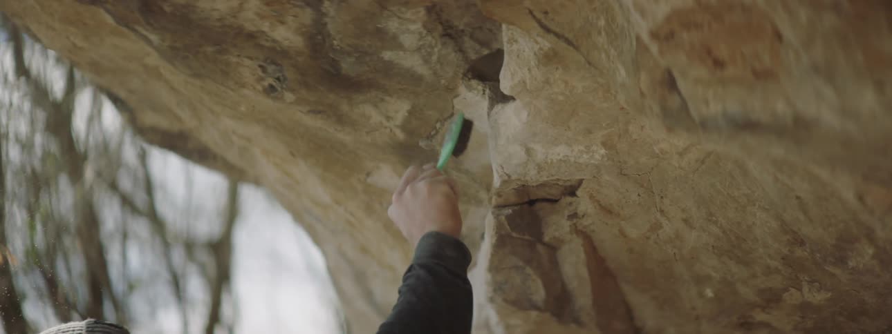 A man using a brush to clean a small ridge on the side of a large rock