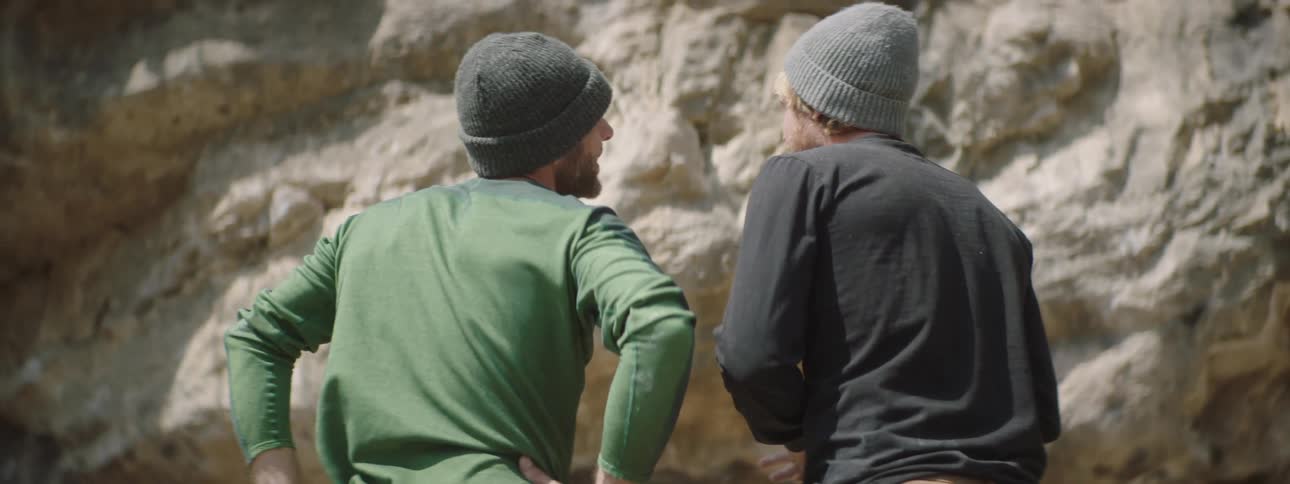 Two men have their backs turned and are talking while looking at a huge rock
