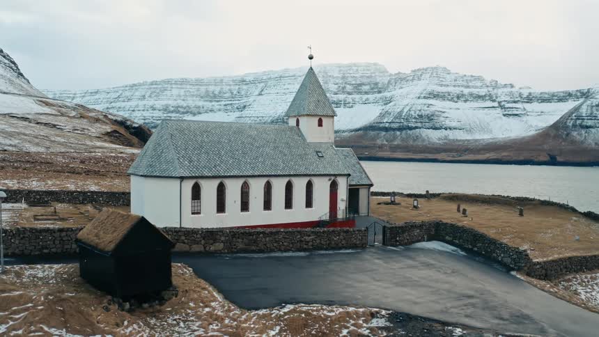 Church with stone wall sits on mountainous coast during winter