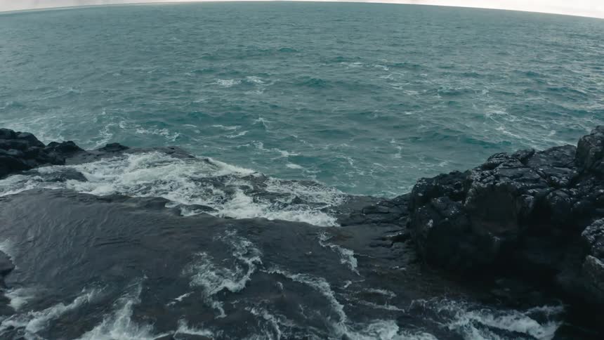 Coastal rocky tidepool and open ocean under cloudy sky