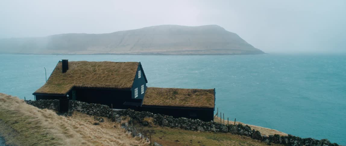 A turf house with two roofs at the base of a hill by the sea