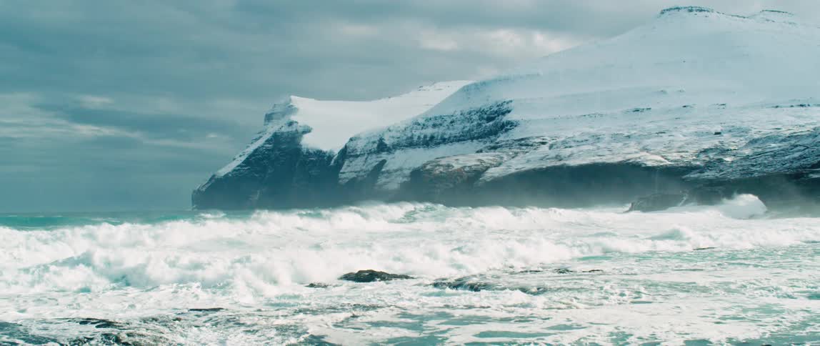 Ocean waves breaking against the coastline with snowy cliffs