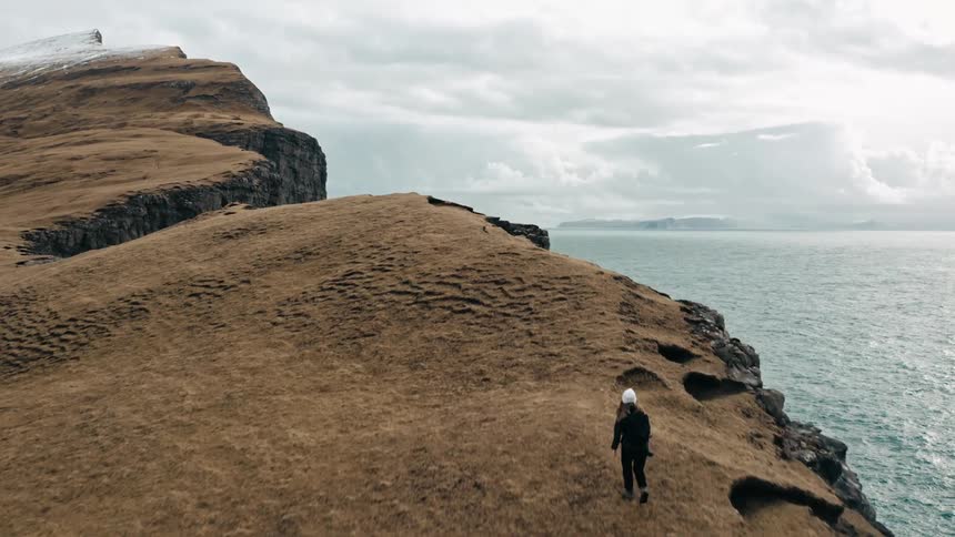 Aerial view of a person walking over a cliff next to the ocean