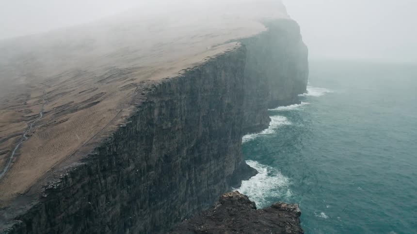 Snow is falling on the fog filled cliffs