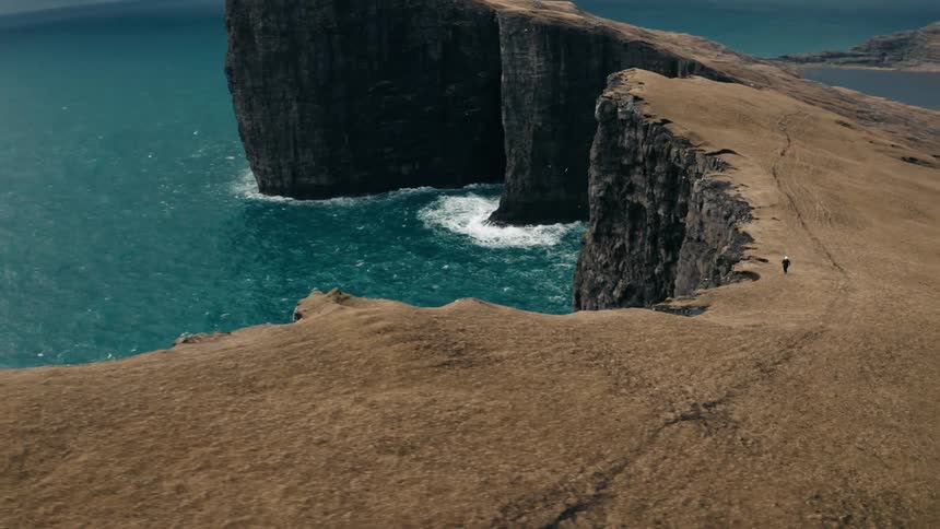 Birds fly by the cliff as a person runs by