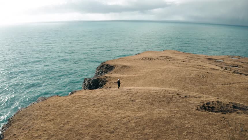 Aerial panorama of a person running on a cliff by the sea