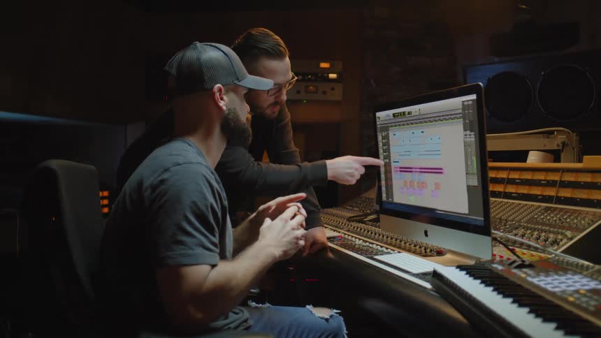 Two men in recording studio consult while viewing monitor