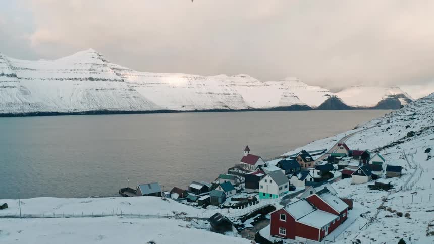 Aerial of a small coastal town in the arctic between mountains