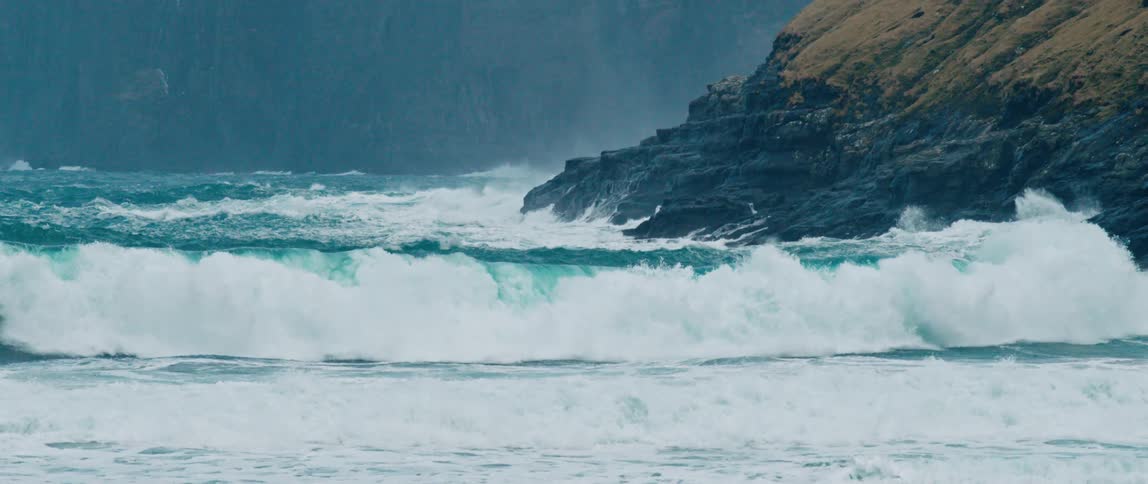Large ocean waves with white crests crash against rocky cliffs