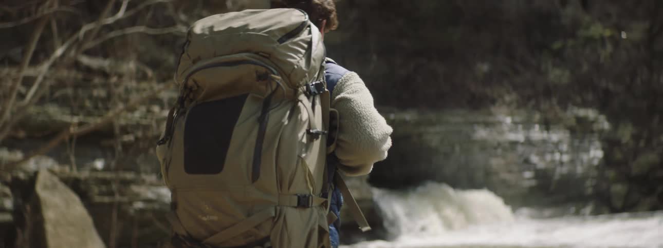 A young man walks with a large backpack over a waterfall