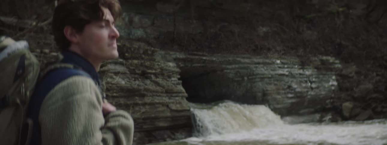 A backpacker stands next to a small waterfall in the mountains