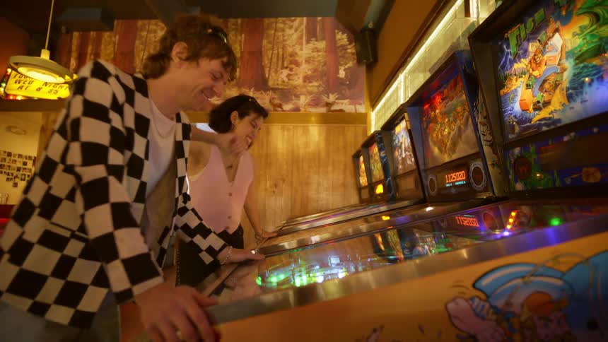 Man and woman in an indoor room playing vintage arcade games