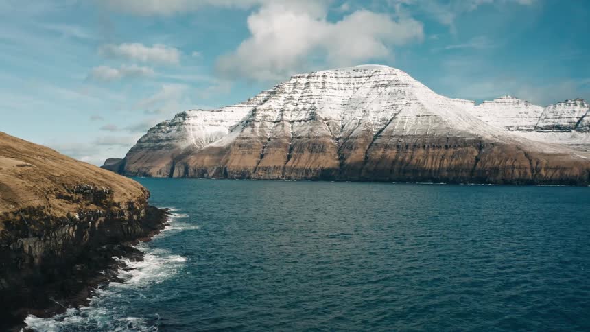 Mountain range with snow on the sea coast during the day