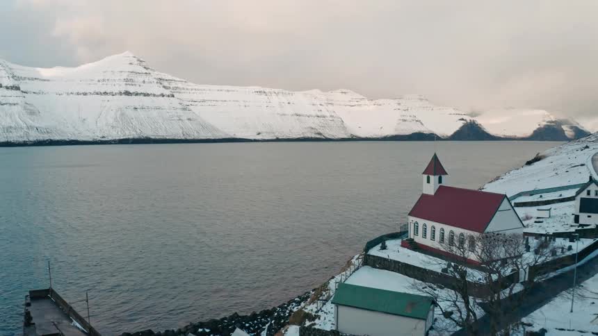 Seaside village surrounded by snowcovered mountains on a cloudy day