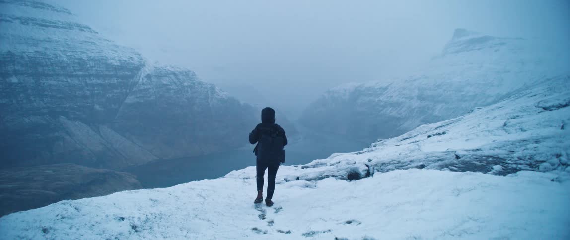 A mountaineer stands on a snowy landscape in the mountains looking at a river