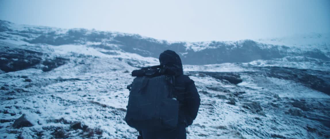 A woman is hiking on a mountain while it snows