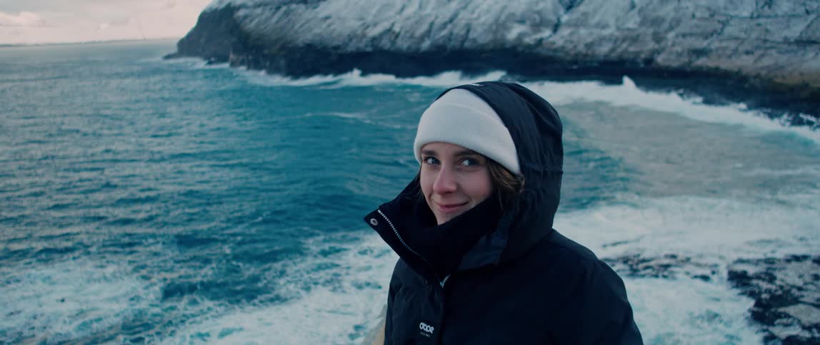 A woman smiles at the camera on the cold shore