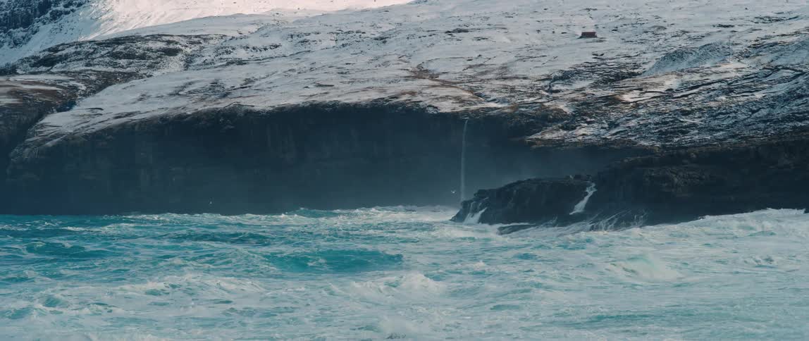 The arctic ocean crashing against cliffs covered in snow