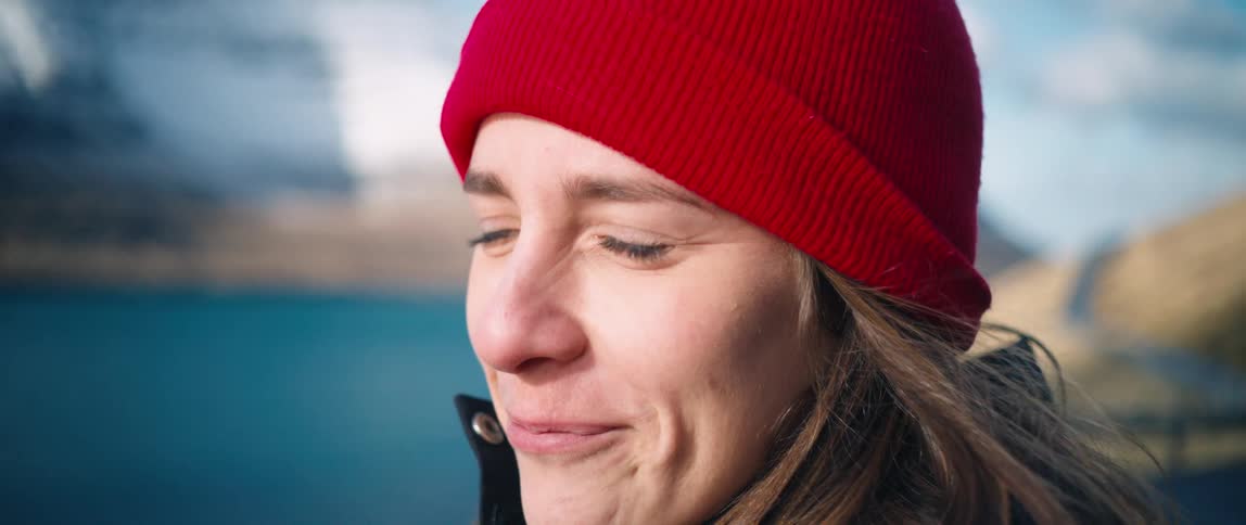 A blonde woman in a red hat is smiling and her eyes are wet