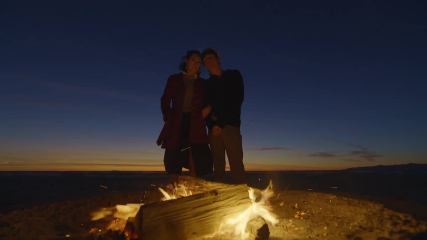 A couple stand by the campfire