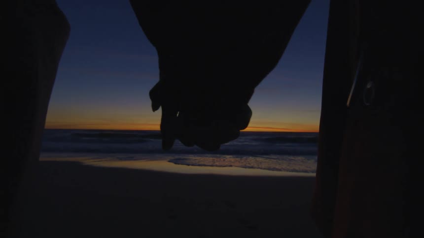 A couple holding hands on the beach at dusk