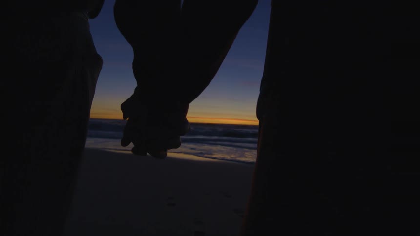 Two people hold hands on the beach