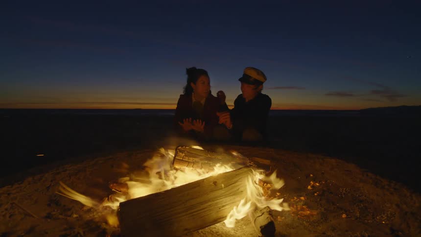 Couple sitting embracing in front of a bonfire at dusk
