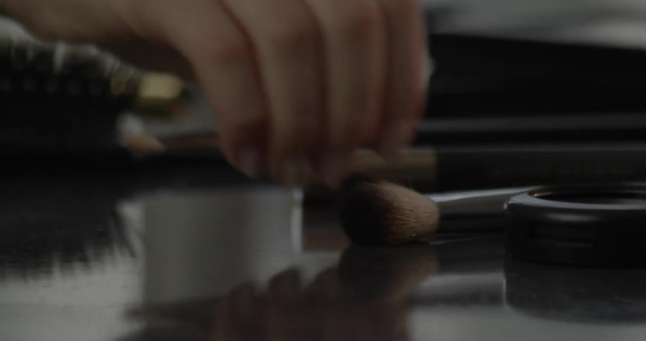 A person picks up a makeup brush from a table