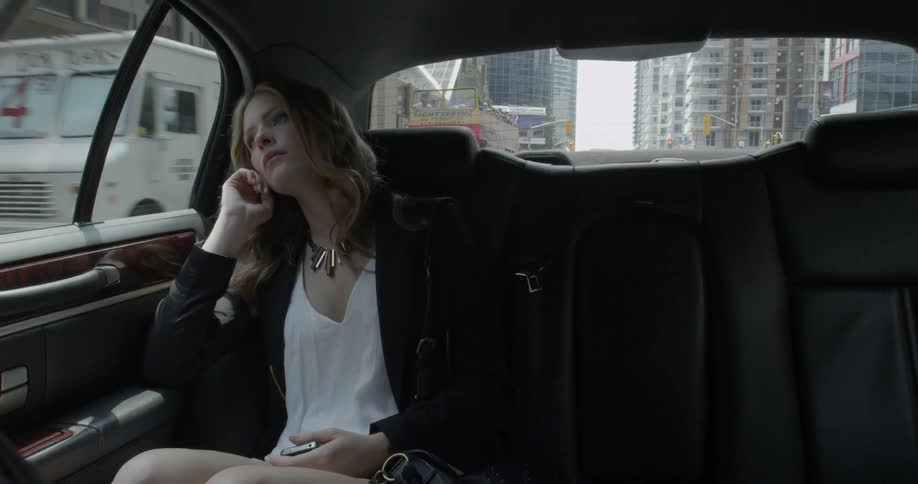 A woman rides in the back of a car on a city street