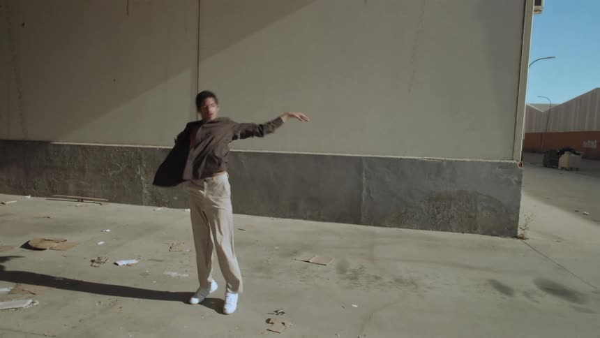 A man performing contemporary dance walks in front of a building