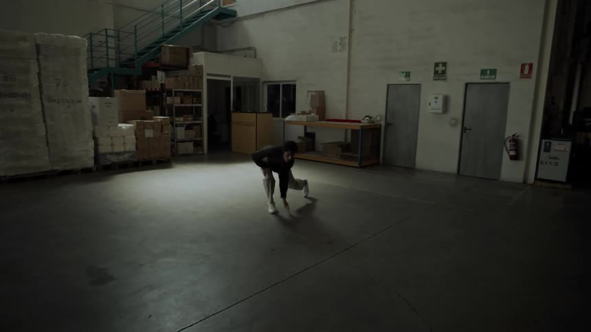 Dancer wearing a black beanie a shirt and gray pants dances in a warehouse