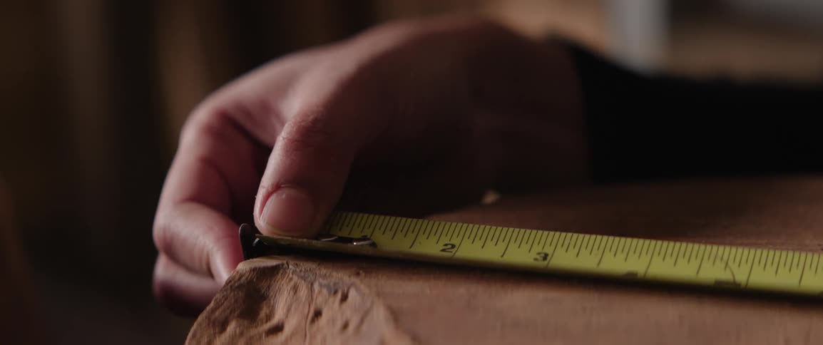Closeup of a persons hand measuring wood with a measuring tape