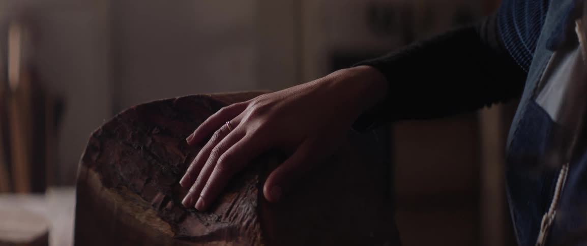 A womans hand and fingers touch a wood carving indoors