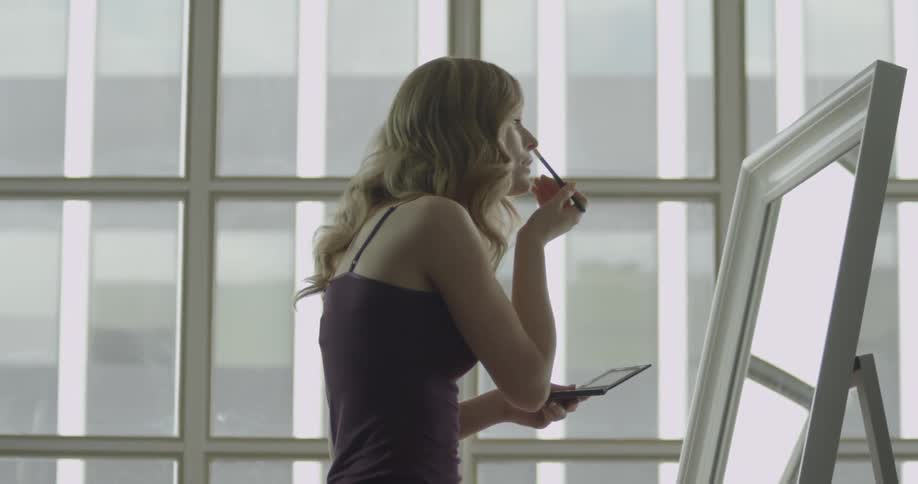 Woman applying makeup while looking in her large mirror
