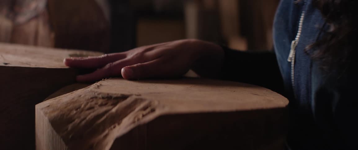 A womans hand feels the texture of raw lumber in a wood shop