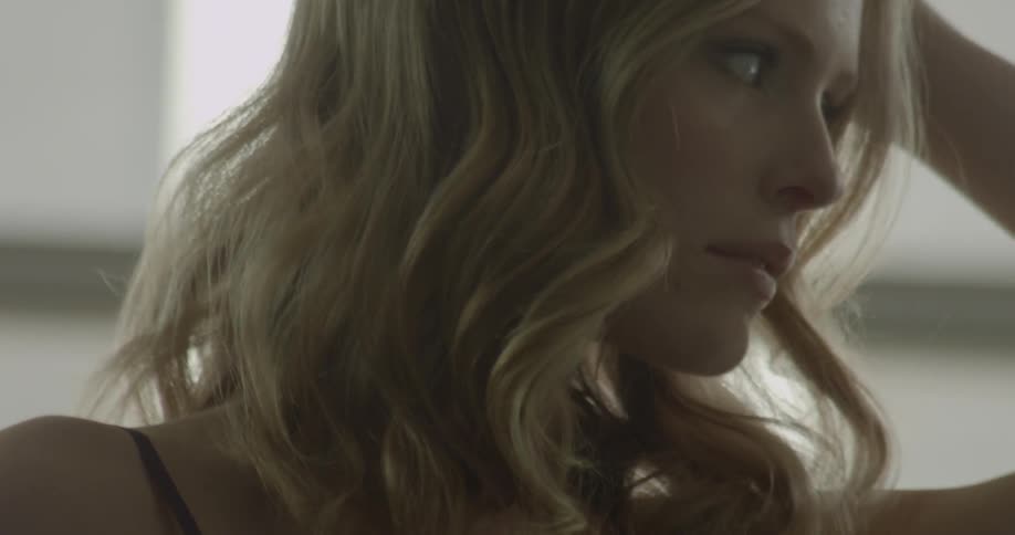 A woman wearing a negligee is turning and running a hand over her hair