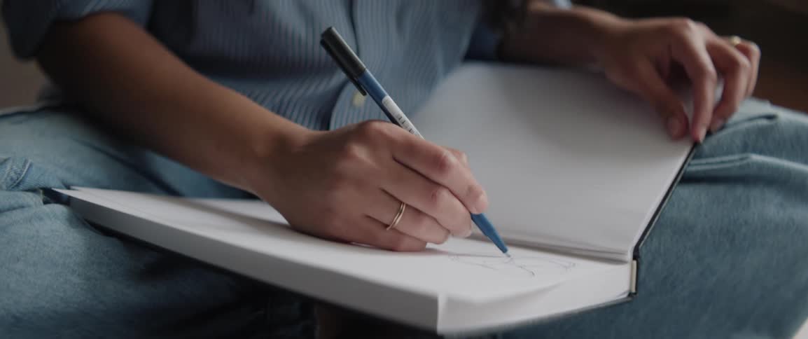 A woman shown from the waist down is sitting on the floor writing in a notebook