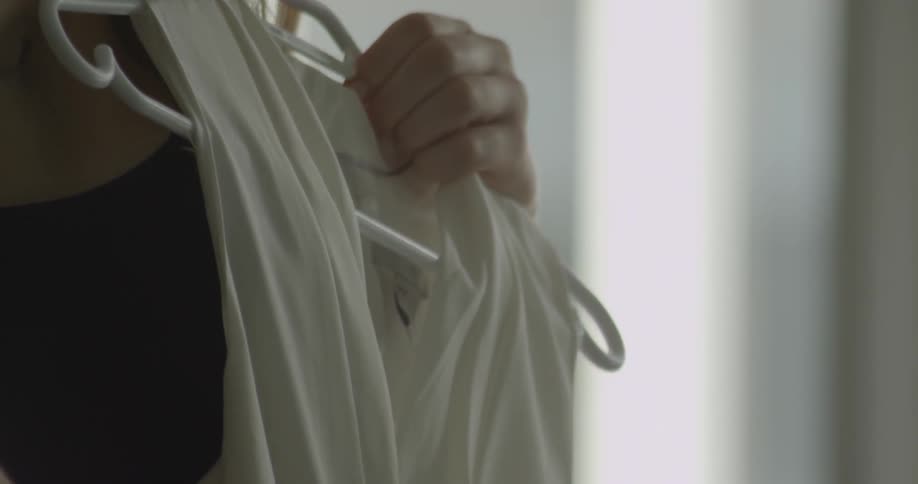 A woman holds two dresses up against her body