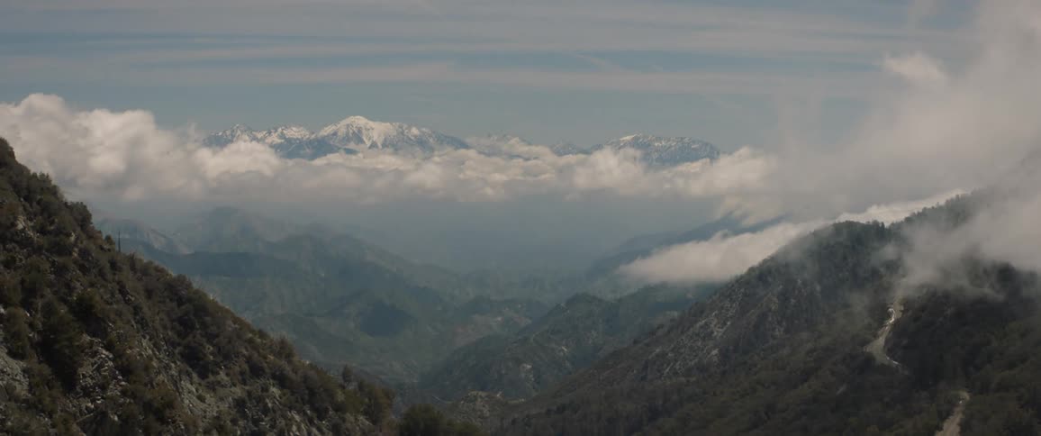 A mountain range with the farthest peaks behind a cloud and covered in snow